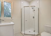 Thumbnail 10 of 16 - A white toilet sits next to a walk-in shower in a bathroom.