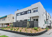 Thumbnail 2 of 5 - A modern white building with a black fence and a green roof.