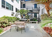 Thumbnail 4 of 13 - A patio with a table and chairs is surrounded by green plants.