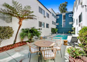 Thumbnail 5 of 13 - A patio with a table and chairs is surrounded by plants and a pool.