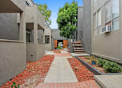 Thumbnail 18 of 19 - A pathway with red bricks leads to a building with a brown door.
