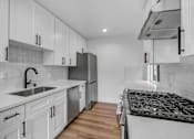 Thumbnail 21 of 29 - A modern kitchen with white cabinets and a black stove top.