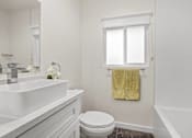 Thumbnail 15 of 29 - A white bathroom with a toilet, sink, and a window with a yellow towel hanging on it.