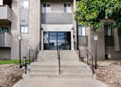 Thumbnail 16 of 29 - A concrete building with a black railing and steps leading to the entrance.
