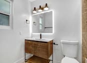 Thumbnail 5 of 29 - A bathroom with a white toilet and a wooden vanity.