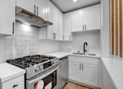Thumbnail 4 of 29 - A modern kitchen with white cabinets and a stainless steel range hood.