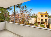 Thumbnail 2 of 14 - A balcony with a view of a yellow building and trees.