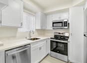 Thumbnail 4 of 14 - A white kitchen with a stainless steel dishwasher and oven.