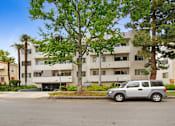 Thumbnail 13 of 14 - A silver car is parked in front of a white apartment building.