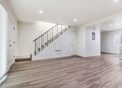 Thumbnail 9 of 21 - A spacious room with wooden flooring and a staircase with a metal railing.