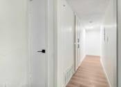 Thumbnail 19 of 23 - A long hallway with white walls and wood flooring.