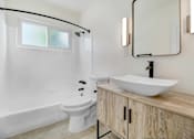 Thumbnail 10 of 23 - A white toilet sits in a bathroom with a wooden vanity and a mirror.