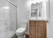 Thumbnail 13 of 22 - A white toilet sits in a bathroom with a wooden cabinet and a glass shower door.