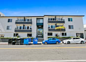 Thumbnail 7 of 37 - A blue car is parked in front of a white building with balconies.