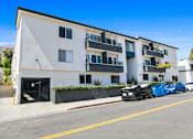 Thumbnail 28 of 37 - A blue car is parked on the street in front of a white building.