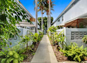 Thumbnail 11 of 11 - A concrete walkway leads between two white buildings with a fence and green plants on either side.