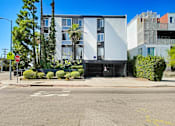 Thumbnail 1 of 4 - A street view of a building with a stop sign and a tree.