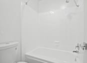 Thumbnail 7 of 11 - A white bathroom with a tub, toilet and sink.