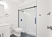 Thumbnail 7 of 11 - A white toilet sits next to a walk-in shower.