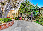 Thumbnail 1 of 6 - A patio with a table and chairs is surrounded by greenery.