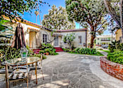 Thumbnail 5 of 6 - A patio with a table and chairs is surrounded by a brick wall and trees.