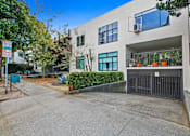 Thumbnail 1 of 4 - A modern building with a black gate and a green bush in front.
