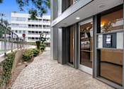 Thumbnail 10 of 24 - A building with a glass door entrance and a brick pathway leading to it.