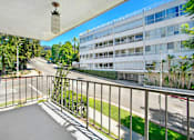Thumbnail 2 of 24 - A balcony with a white railing and a hanging light fixture overlooks a street with a white building in the background.