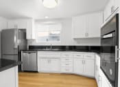 Thumbnail 1 of 11 - a kitchen with white cabinets and black counter tops and a stainless steel refrigerator
