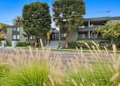 Thumbnail 8 of 12 - A modern house with a grey exterior and a balcony is surrounded by tall grass and trees.