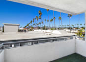 Thumbnail 2 of 13 - A balcony with a view of palm trees and a building.