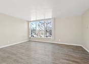 Thumbnail 9 of 28 - Empty room with a large window and wooden flooring.