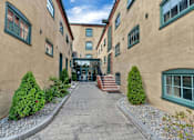 Thumbnail 3 of 39 - A long, narrow alleyway between two tan buildings with green trim and steps leading to the entrance.