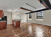 Thumbnail 1 of 39 - A room with wooden floors and a kitchen area with brown cabinets.