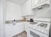 Thumbnail 2 of 25 - A white kitchen with a stove top oven and a sink.