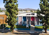 Thumbnail 1 of 7 - A building with a blue and pink facade is surrounded by trees.