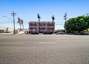 Thumbnail 7 of 17 - A street view with a building in the background and cars parked on the side of the road.