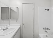 Thumbnail 24 of 25 - A white bathroom with a sink, mirror, and bathtub.
