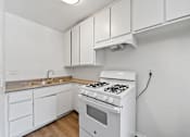 Thumbnail 18 of 25 - A white kitchen with a stove and cabinets.