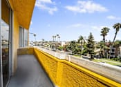 Thumbnail 15 of 19 - A yellow building with a balcony overlooking a street with palm trees.