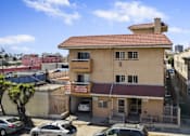 Thumbnail 10 of 10 - A two-story building with a red roof is surrounded by parked cars.