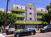 Thumbnail 2 of 27 - A black car is parked in front of a grey and green building.