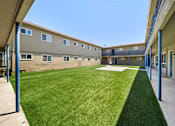 Thumbnail 2 of 10 - A grassy courtyard is surrounded by apartment buildings.