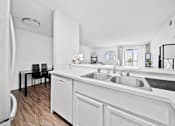 Thumbnail 9 of 12 - A white kitchen with a black chair and a white fridge.