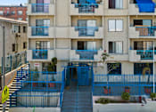 Thumbnail 2 of 12 - A blue fence surrounds a building with a staircase leading to the entrance.