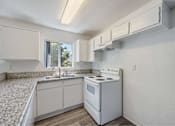 Thumbnail 13 of 15 - A white kitchen with a stove, sink, and cabinets.
