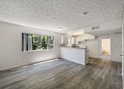 Thumbnail 4 of 15 - A spacious kitchen and living room with wood flooring and white walls.