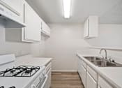 Thumbnail 33 of 38 - A white kitchen with a stove, sink, and cabinets.