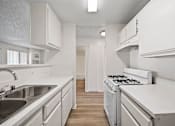 Thumbnail 29 of 38 - A white kitchen with a stove, sink, and cabinets.