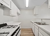 Thumbnail 23 of 38 - A white kitchen with a stove, sink, and cabinets.